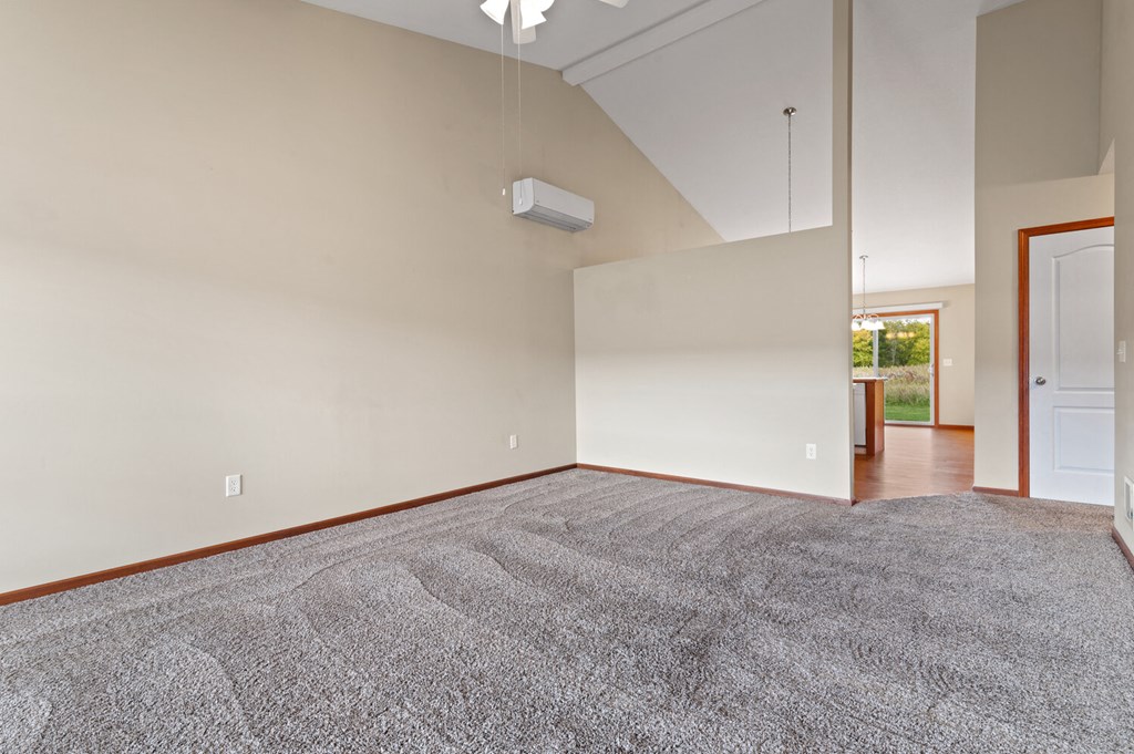 an empty living room with carpet and a door to a kitchen