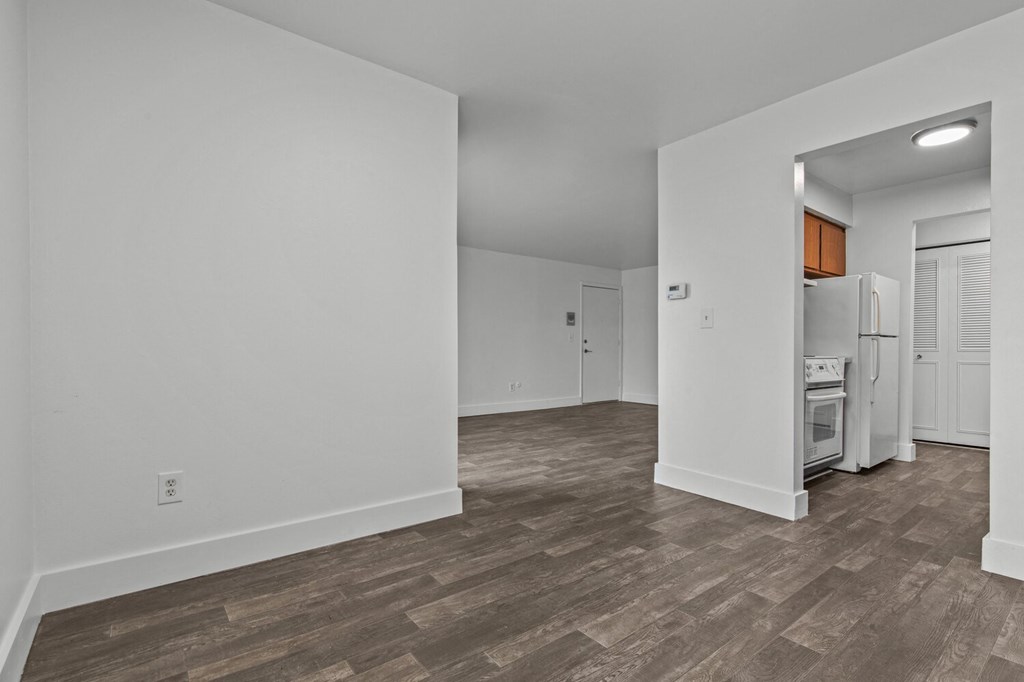 the living room and kitchen of an apartment with white walls and wood flooring