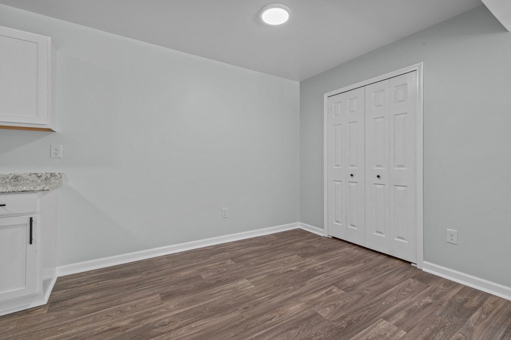 an empty living room with a door to a closet and a kitchen