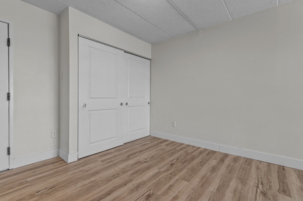 the living room of an apartment with white walls and wood flooring