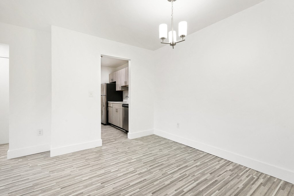 the living room and kitchen of an apartment with white walls and wood flooring