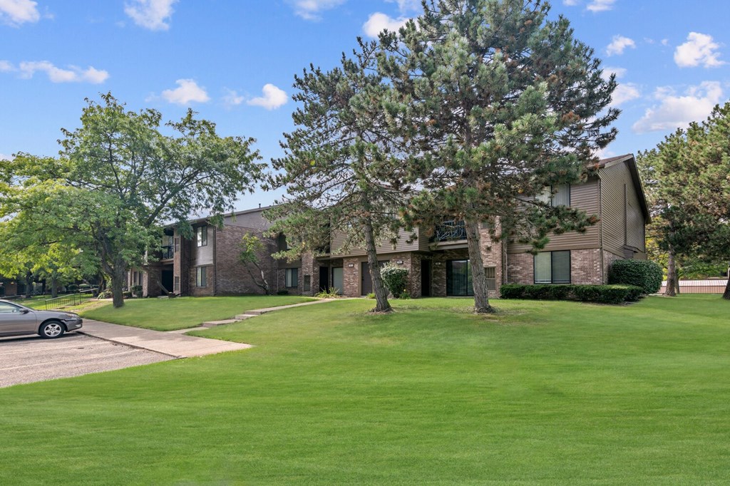 an apartment building with a lawn and trees in front of it