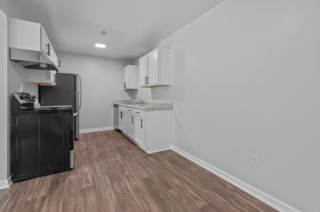 an empty kitchen with white cabinets and a black refrigerator and stove