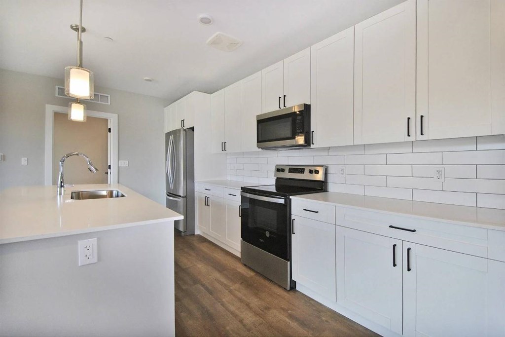 A kitchen with white cabinets and a black microwave above the stove.