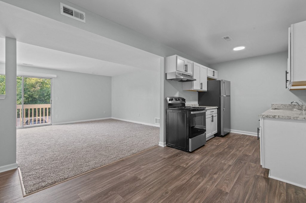 an empty living room with a kitchen with a stove and refrigerator