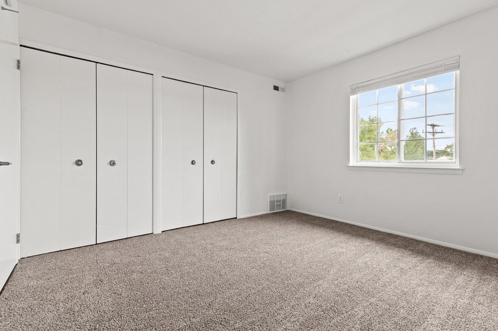 a room with carpet and white closets and a window