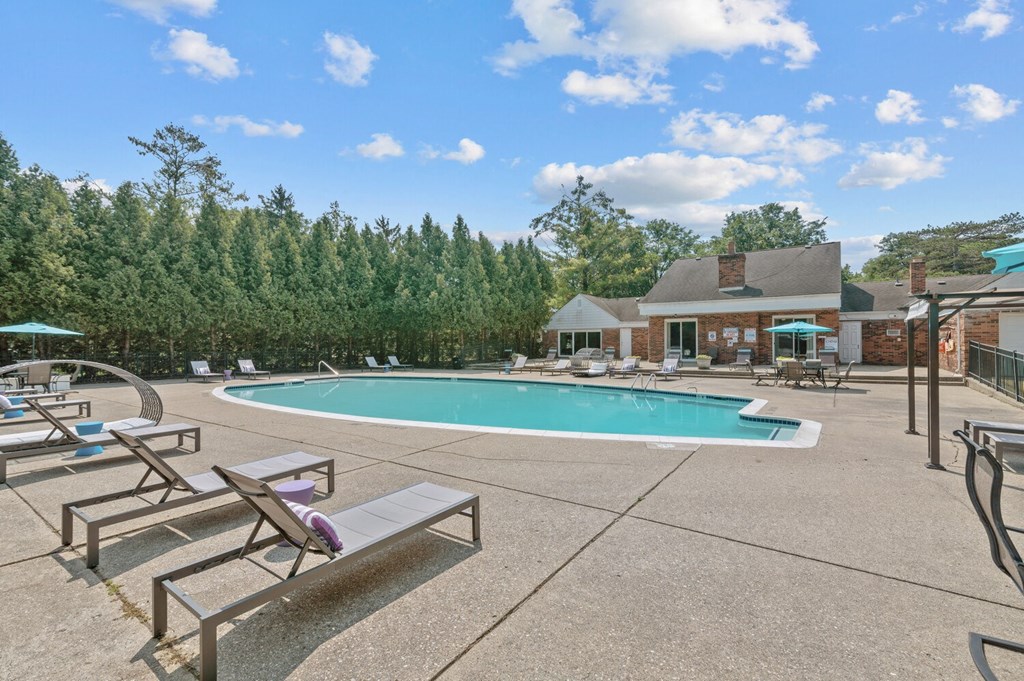 a swimming pool with chaise lounge chairs and umbrellas at Apple Ridge Apartments - Livonia, MI, Livonia
