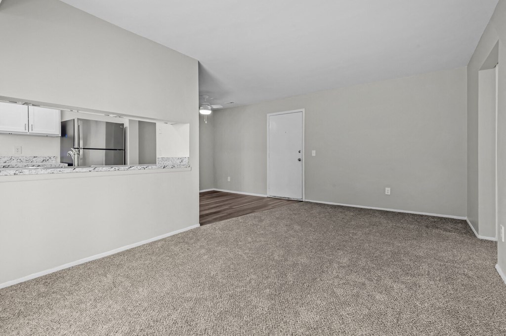 the living room and kitchen of an apartment with white walls and a carpeted floor