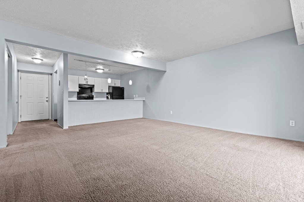 the living room and kitchen of an apartment with carpeted flooring and a counter  at Fairfax Apartments - Lansing, MI, Lansing, MI, 48917