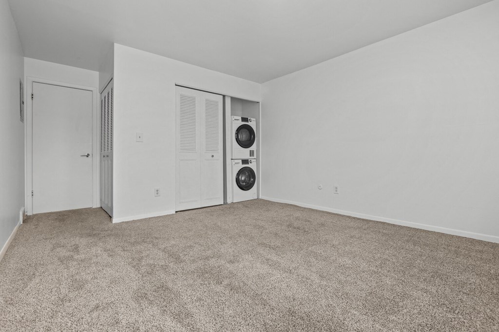 an empty living room with white walls and carpet and a washer and dryer