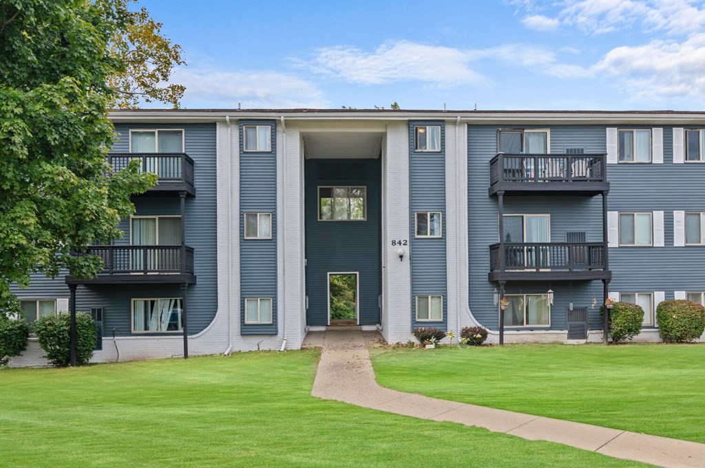 the view of a blue apartment building with a green lawn