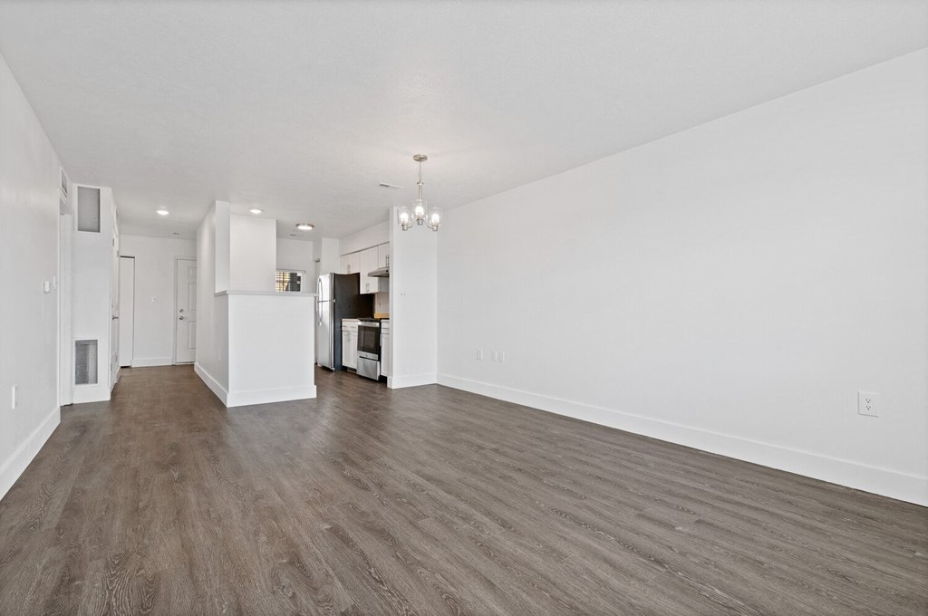 a spacious living room with white walls and hardwood floors