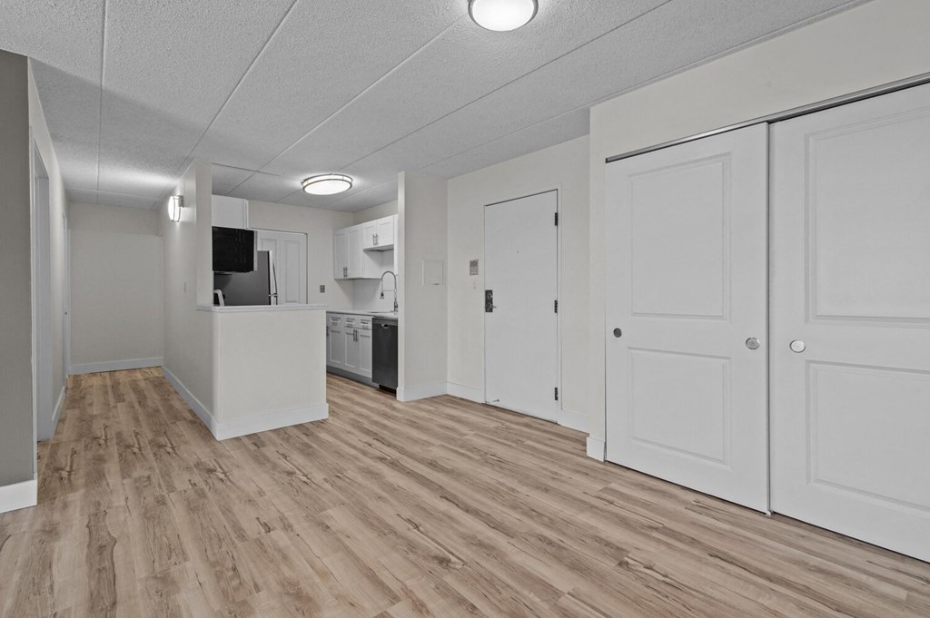 an empty living room and kitchen with white walls and wood flooring