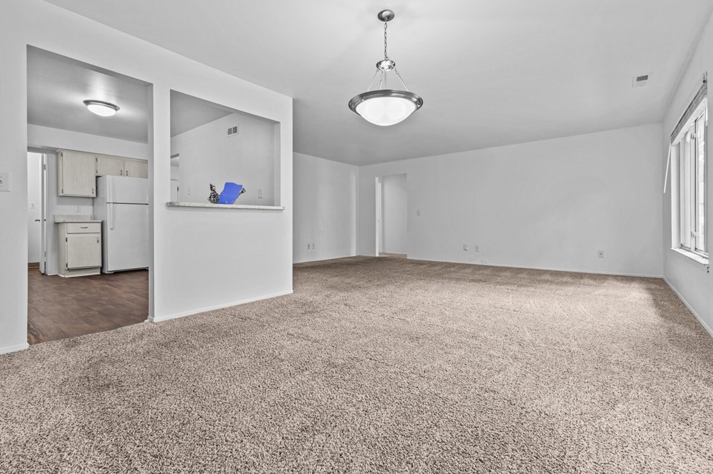 an empty living room with white walls and carpet and a kitchen at Edge At Farmington Hills - Farmington Hills, MI, Michigan