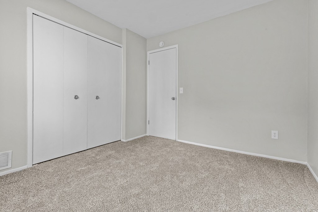 an empty bedroom with white doors and carpeting
