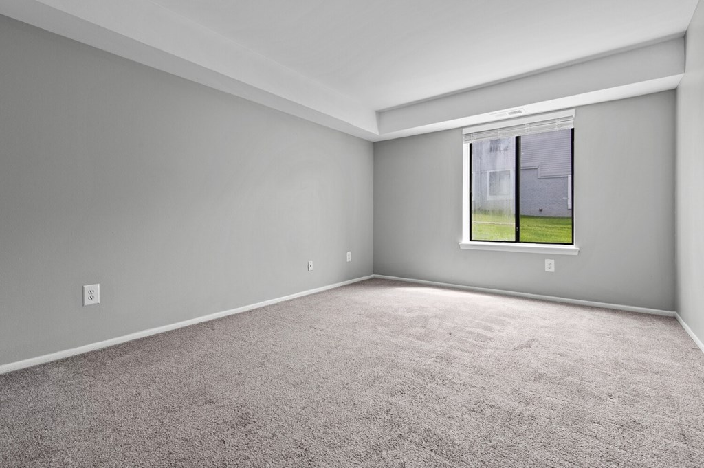 A room with a carpeted floor and a window showing a view of a house.