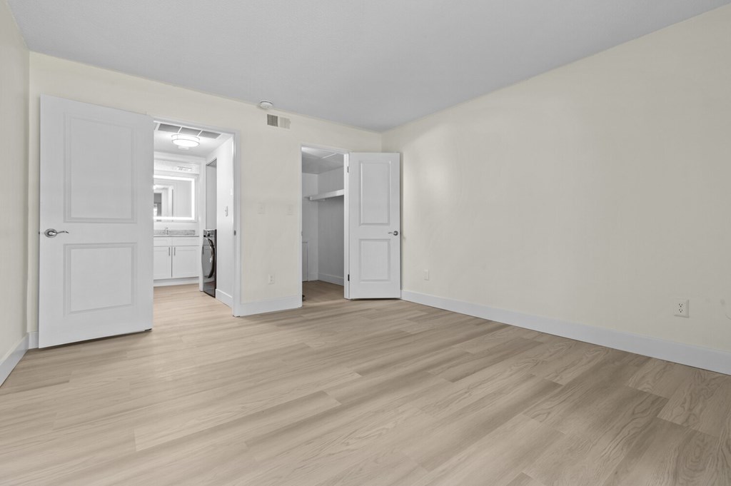 A room with white walls and wooden flooring with a door and a cabinet.