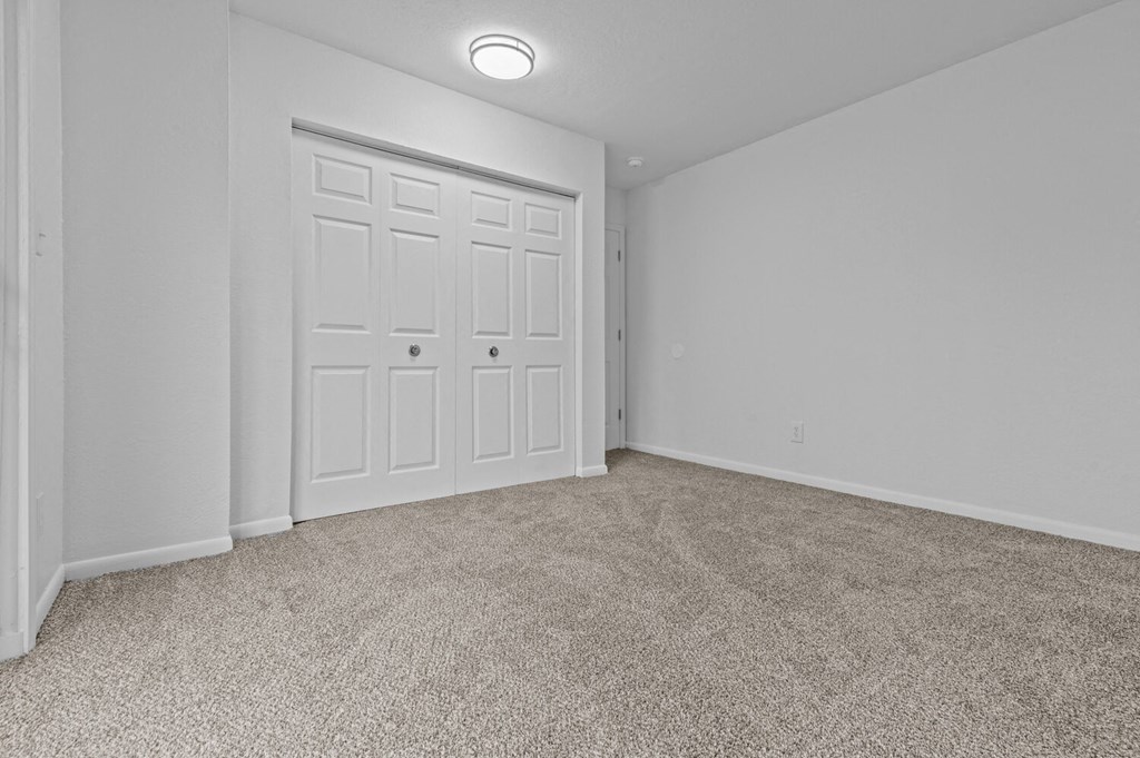 an empty bedroom with white doors and carpeting
