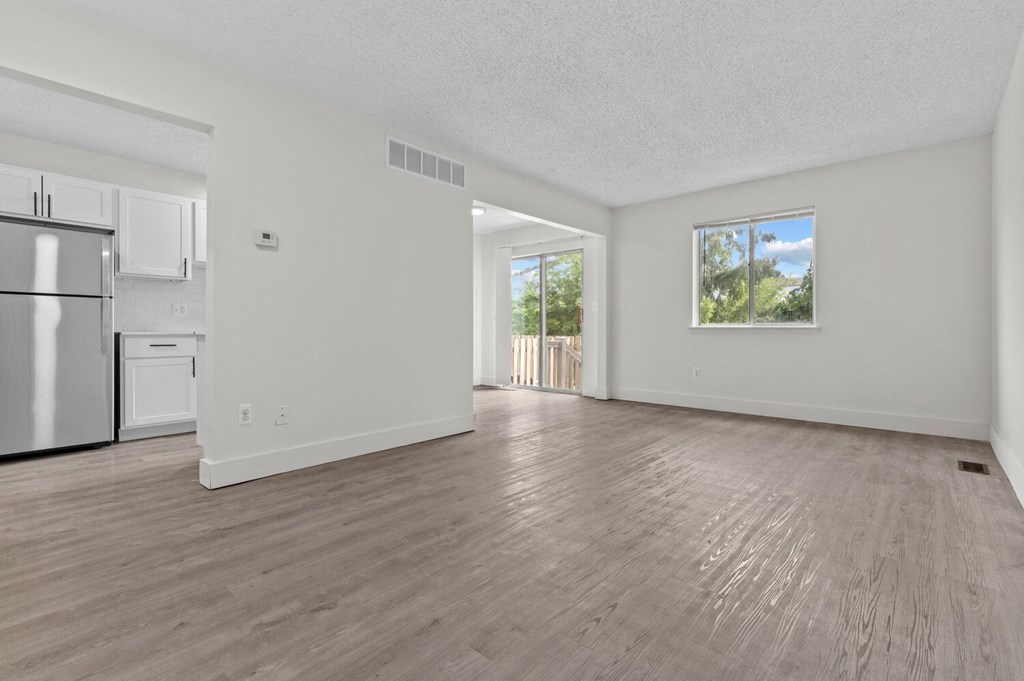 the living room and kitchen of an apartment with white walls and wood floors at Sterling Lake - Sterling Heights, MI, Sterling Heights