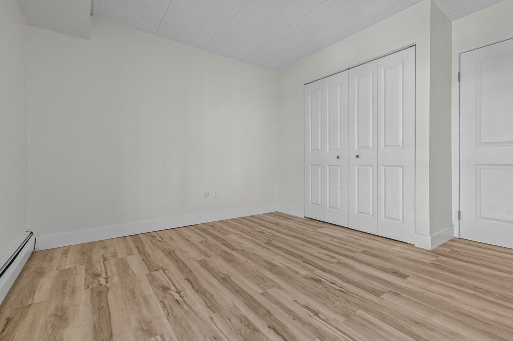 the living room of an apartment with white walls and wood flooring