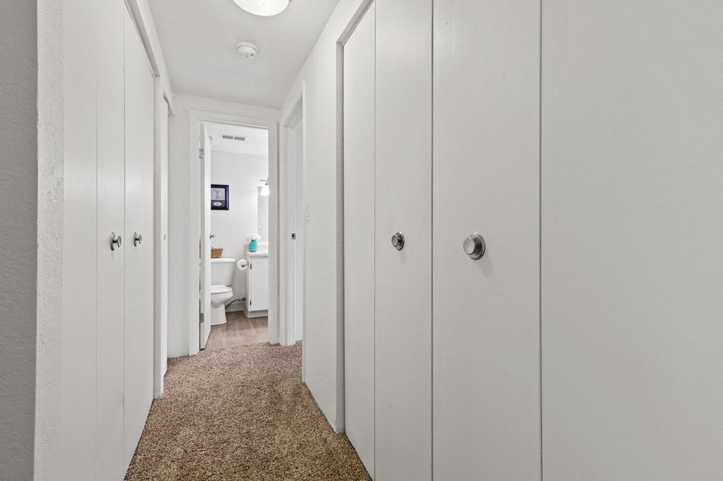a long white hallway with white closets and a carpet
