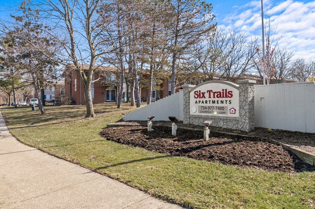 a sign for ski trails apartments in front of a sidewalk and trees