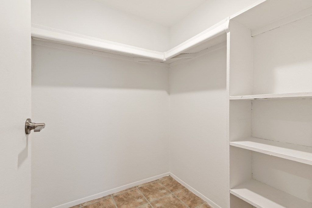a walk in closet in a white room with shelves