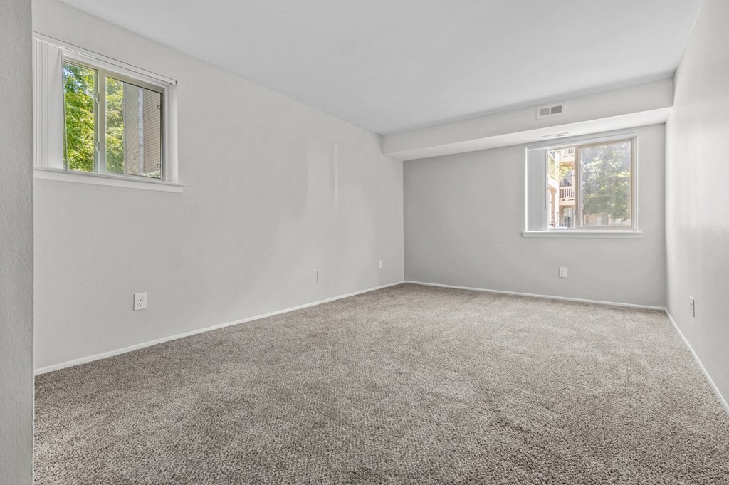 an empty bedroom with carpet and two windows
