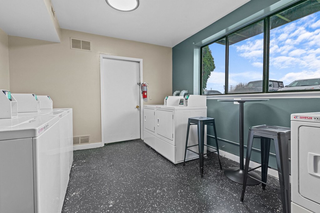 a laundry room with washing machines and a counter with two stools  at Park On Canal Apartments, Clinton Twp, MI
