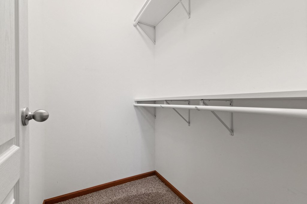 a walk in closet with a white wall and a hanging rack on the wall