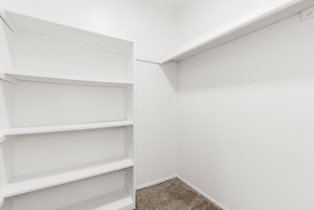 an empty closet with white shelves and white walls