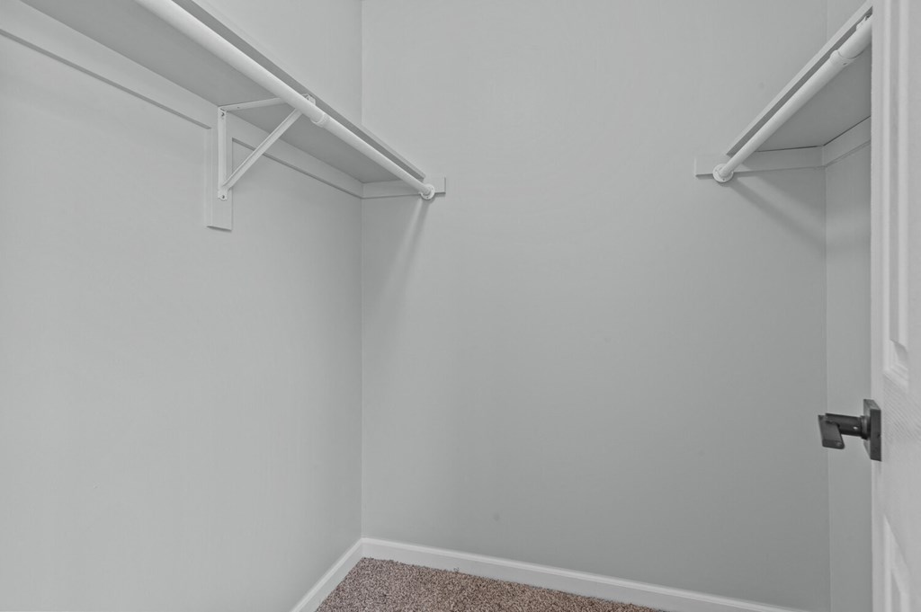 room with white walls and a closet with white shelves and a door