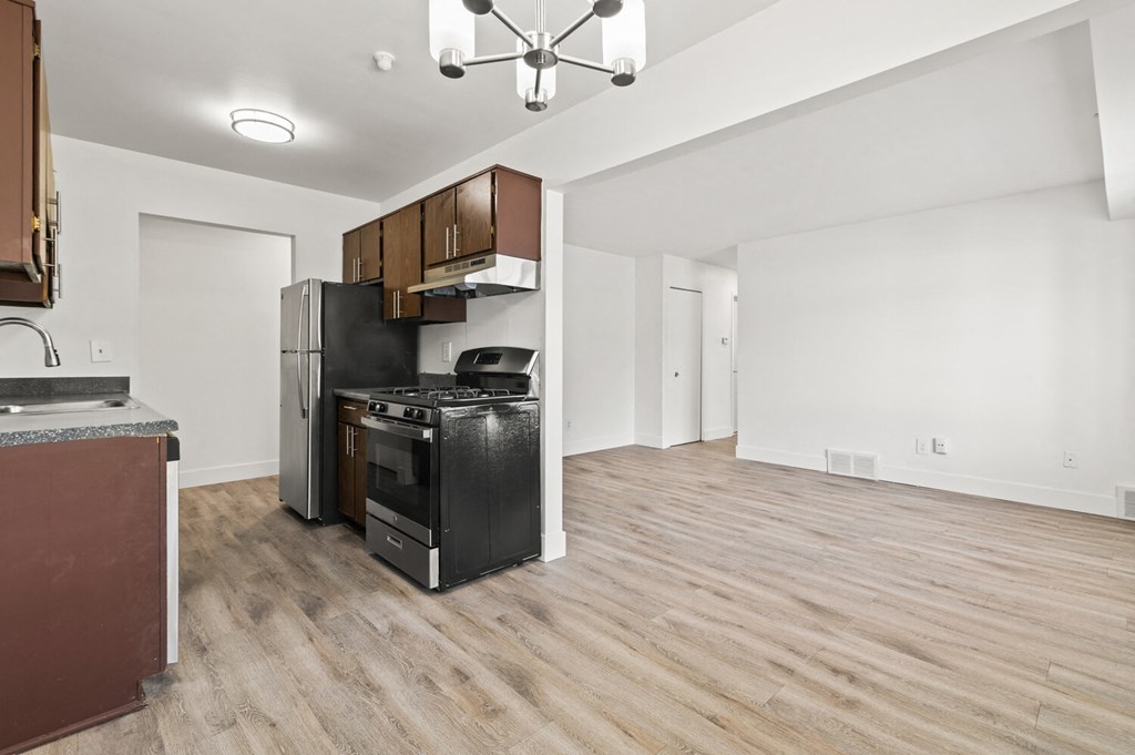 an empty living room with a kitchen with a stove and refrigerator