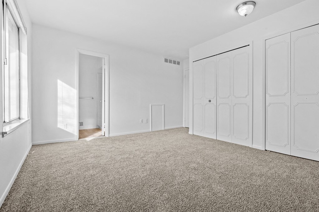 a bedroom with white walls and carpet and white closets