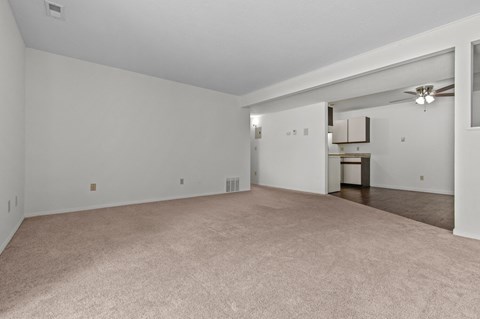 the spacious living room and dining room with white walls and carpet