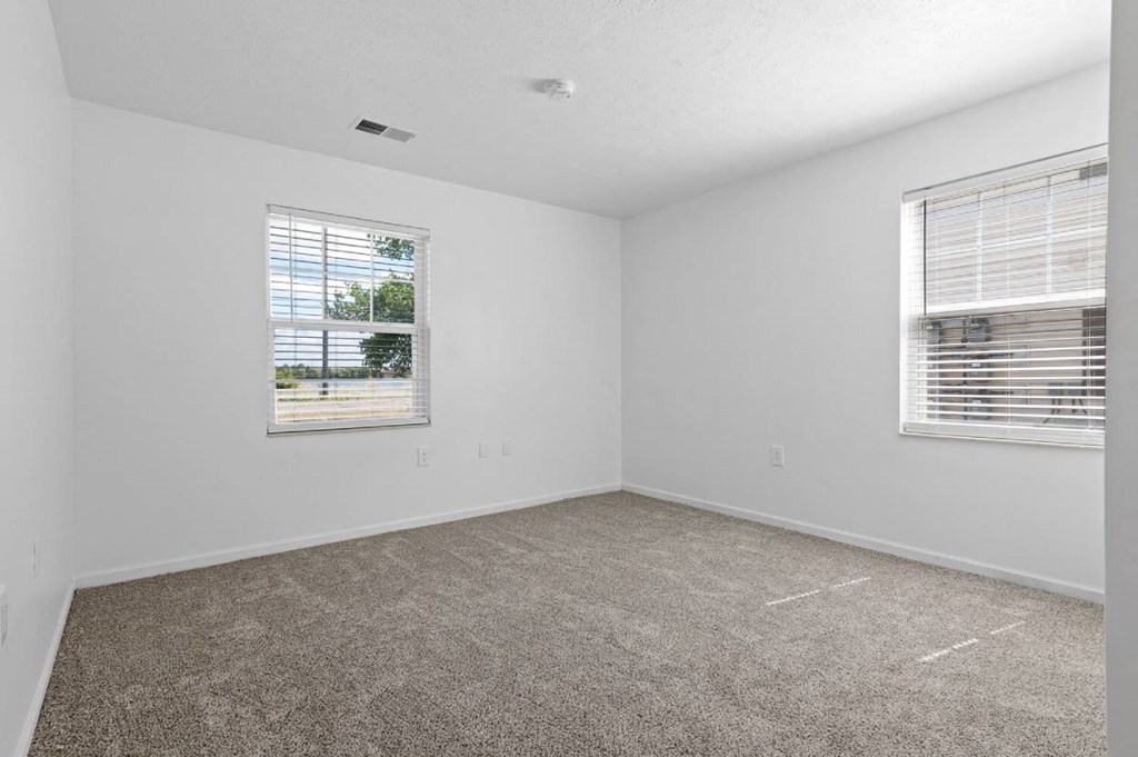 a bedroom with two windows and a carpeted floor