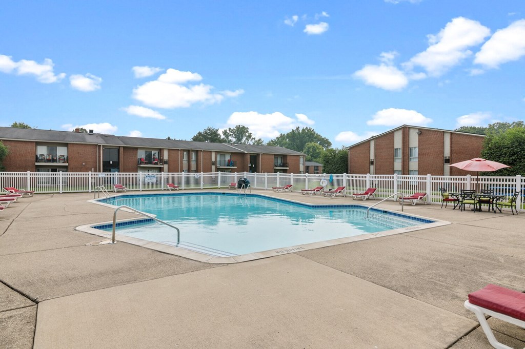 a swimming pool with chaise lounge chairs and tables in front of a brick building