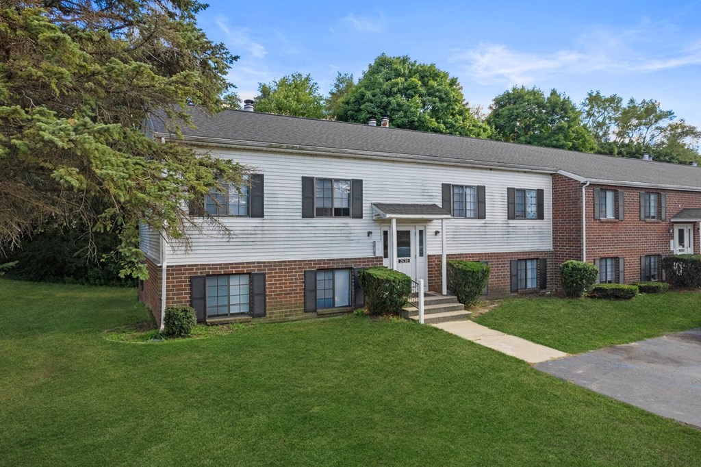 the front of a white house with a green lawn and trees