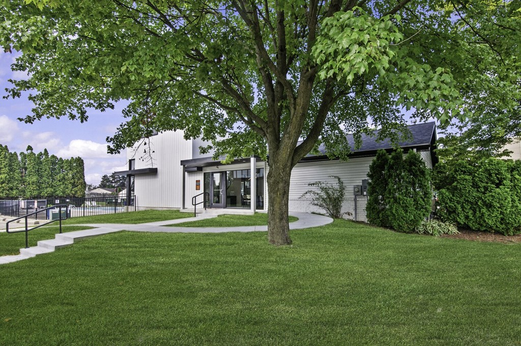 A tree in front of a building with a white fence in the background.