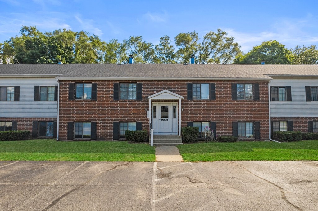 a brick apartment building with a white front door and green grass