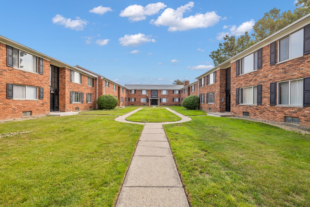 an exterior view of an apartment building with a grass yard and sidewalk