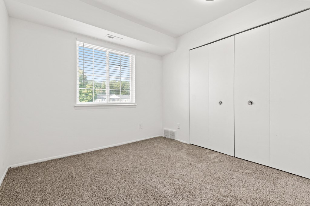 a bedroom with white walls and carpet and a window