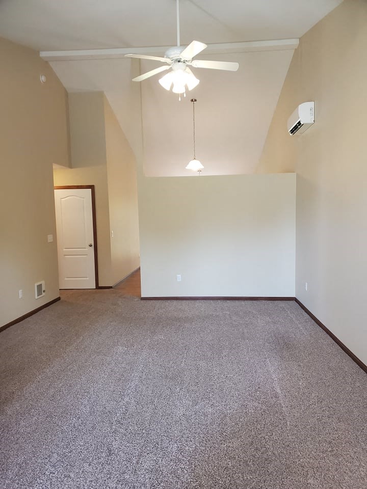 an empty living room with a ceiling fan and a white wall