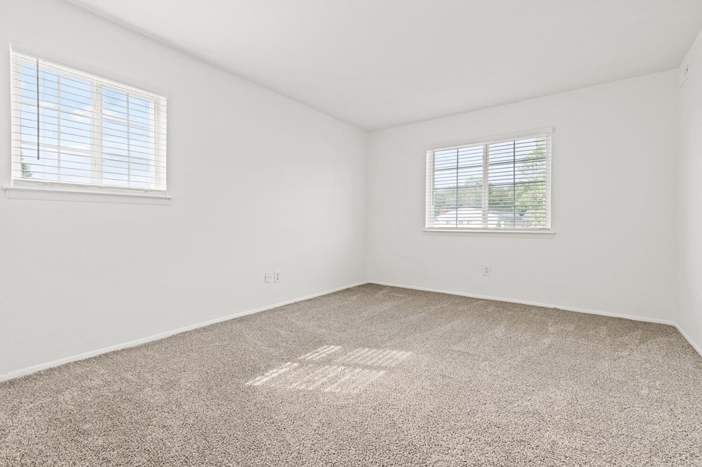 an empty room with carpet and two windows