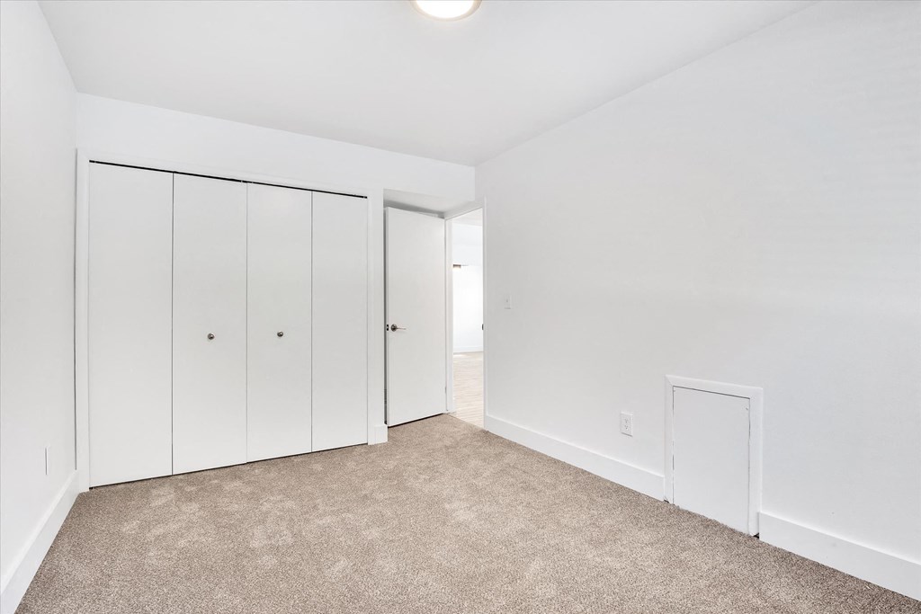 a bedroom with white walls and carpet and white closets