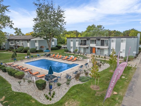 A pool surrounded by chairs and trees with apartment buildings in the background.
