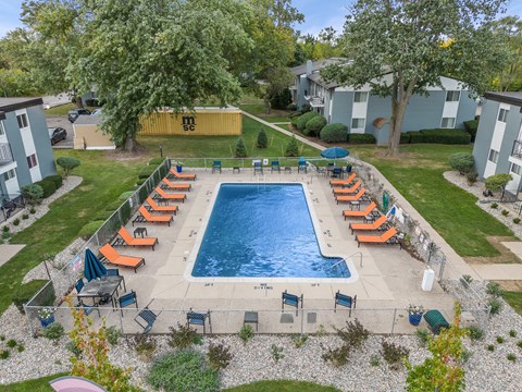 A pool surrounded by orange lounge chairs and green trees.
