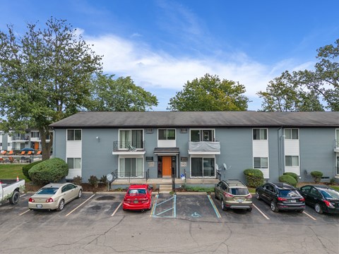 A parking lot in front of a grey apartment building with cars parked in designated spots.