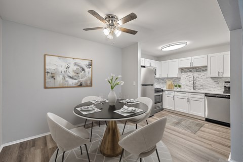 A modern dining room with a table set for two and a kitchen in the background.