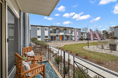 A balcony with two chairs and a table overlooks a grassy area with buildings in the background.